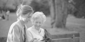 elderly woman and young woman sitting together bench outdoors