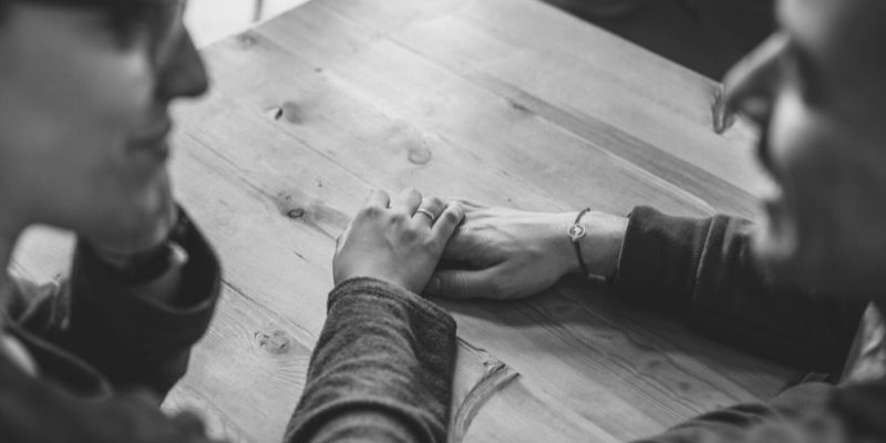 A black and white image of a couple holding hands across a table.