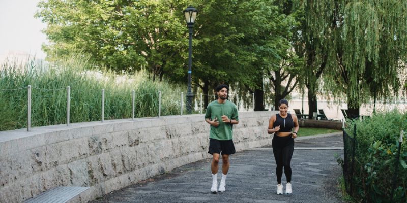 A young couple jogs along a paved trail in a lush, green park.